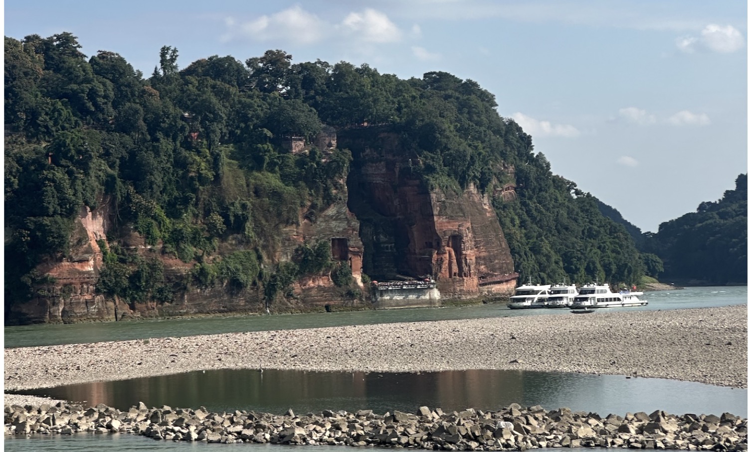 The Leshan Giant Buddha carved into red cliffs beside the river